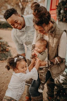 a man and woman holding two small children in front of a christmas tree