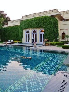 an outdoor swimming pool in front of a large house with ivy growing on the walls