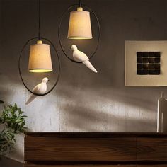 two white birds sitting on top of a wooden dresser next to a wall mounted light fixture