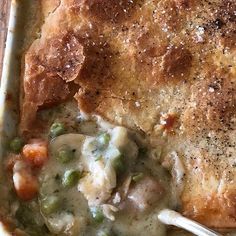 a casserole dish with chicken, peas and potatoes in gravy on a wooden table