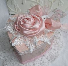 a pink rose sitting on top of a heart shaped box with lace around the edges