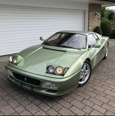 a green sports car is parked in front of a garage with a white door and brick driveway