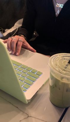 a woman sitting at a table with a laptop computer on her lap and a drink in front of her