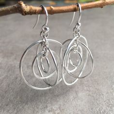 "These unique dangle hoop earrings are handmade with solid, nickel free sterling silver. There are four circles that are linked in such a way that they give the earrings a kind of 3-d sphere of movement. Each circle is individually soldered, hammered slightly for texture and polished to a high shine to reflect the light beautifully. These are designed to be super lightweight and comfortable to wear, perfect for everyday! * The largest circle measures 1\" across and the earrings measure a total o Modern Wire Wrapped Dangle Hoop Earrings, Nickel-free Silver Plated Dangle Hoop Earrings, Silver-plated Hoop Earrings, Silver Plated Hoop Earrings, Wire Wrapped Sterling Silver Hoop Earrings, Modern Silver Wire Wrapped Hoop Earrings, Silver Wire Wrapped Small Hoop Earrings, Small Hoop Wire Wrapped Silver Earrings, Modern Wire Wrapped Round Hoop Earrings