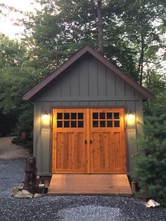 a small shed with two doors and lights on the front door is surrounded by trees