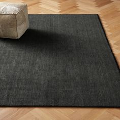 a black area rug on top of a wooden floor next to a chair and ottoman