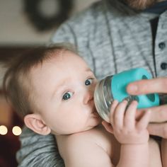 a man holding a baby in his arms and drinking out of a bottle with a sippy cup