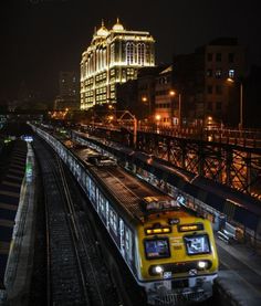 a train is traveling down the tracks in front of a large building at night time