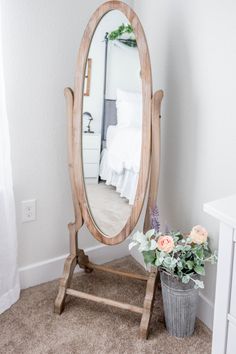 a mirror sitting on top of a wooden stand next to a potted plant in front of a bed