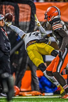 two football players colliding for the ball in front of an orange and black referee