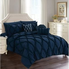 a bed with blue comforter and pillows in a room next to a white dresser