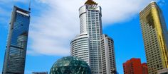 some very tall buildings in the city with blue sky and clouds behind them on a sunny day