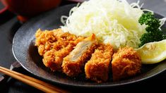 a black plate topped with fried chicken and broccoli next to chopsticks