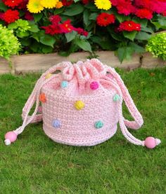 a pink crocheted bag with pom poms on it sitting in the grass