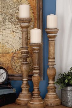 three candles are sitting on a table next to an old world map and a clock