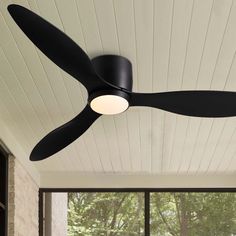 a black ceiling fan sitting on top of a wooden floor next to a large window