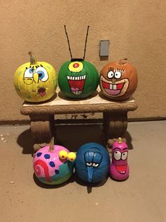 four painted pumpkins sitting on top of a wooden bench with faces drawn on them