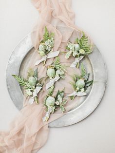 a plate with flowers and greenery on it next to a pink cloth draped over the edge