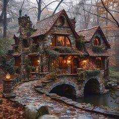 a stone house in the woods surrounded by trees and leaves with lights on it's windows