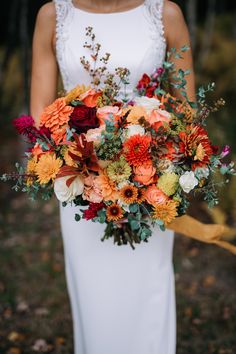 a woman holding a bouquet of flowers in her hand and wearing a white dress with an orange sash