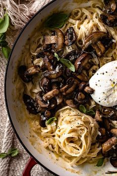 a pan filled with pasta and mushrooms on top of a table next to a cloth