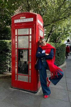 a woman leaning against a telephone booth on the sidewalk with her arms wrapped around her head