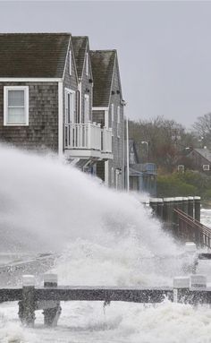 a large wave crashes into the street in front of houses