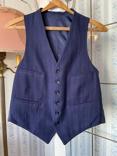 This tailored vest is made from a wool blend in dark royal/navy blue, with widely spaced light blue and beige pinstripes. It has the original buttons in the front and four front pockets, and is fully lined. There are no labels. The measurements, taken with the vest lying flat. are: shoulder to shoulder, 11 inches; armpit to armpit, 19 inches; length, 24 inches in front and 20 inches in back; bottom edge, 17 inches. In very good condition. Pinstripe Waistcoat, Long Beige Coat, Blue Waistcoat, Royal Navy Blue, Tailored Vest, Blue Vest, Beige Coat, Vest Waistcoat, Blue Vests