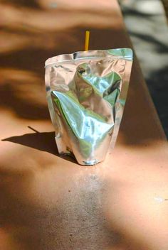 a plastic bag with a yellow straw sticking out of it sitting on a concrete bench