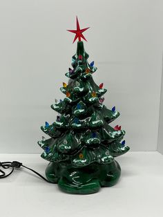 a small green ceramic christmas tree with lights on it's base and a red star on top