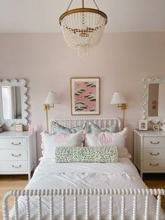 a white bed sitting under a chandelier next to a dresser with drawers and lamps