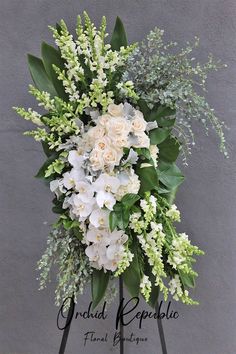 white flowers and greenery are arranged on an easel