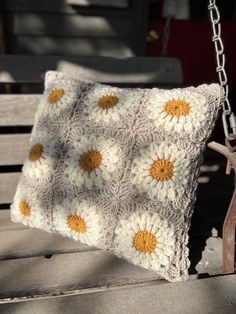 a crocheted pillow hanging from a chain on a wooden bench with a tree in the background