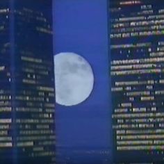 the full moon is seen in front of some tall buildings