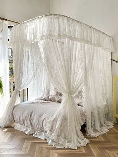 a canopy bed with sheer curtains on the top and bottom, in a room with wooden floors