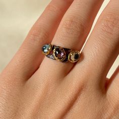 This 925 Sterling Silver adjustable band ring is purely handmade. Black Sterling Silver band part is Rhodium plated and bezels around the crystals are 18k Gold plated. Natural faceted Blue Topaz, Amethyst and Green Tourmaline crystals are used. The size of the ring can be adjusted easily by hand. Blue Topaz: * color blue carries soothing energy and brings peace * helps releasing tensions * stimulates creativity * teaches self-love and self-realization * deflects negative energy * provides emotio Tourmaline Three-stone Ring As A Gift, Tourmaline Three-stone Ring For Gift, Tourmaline Three-stone Ring Perfect For Gifting, Tourmaline Three Stone Ring Perfect As A Gift, Tourmaline Multi-stone Promise Ring, Unique Multi-stone Blue Topaz Ring, Fine Jewelry Multi-stone Topaz Rings, Fine Jewelry Topaz Multi-stone Rings, Unique Topaz Rings With Gemstone Accents