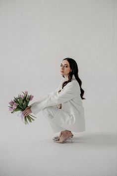 a woman kneeling down with a bouquet of flowers in her hand and looking up at the sky