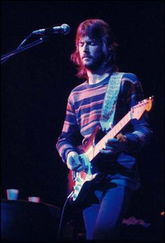 a man with long hair playing an electric guitar in front of a microphone on stage