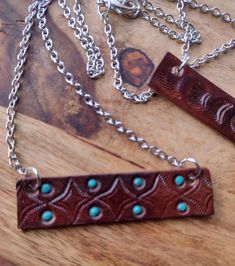 two necklaces with turquoise stones on them sitting on a wooden table next to a chain