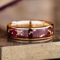 a wedding band with red and gold flecks sits on top of a wooden table