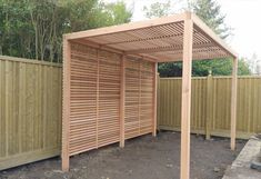 a wooden pergolated area in the middle of a fenced in area with trees