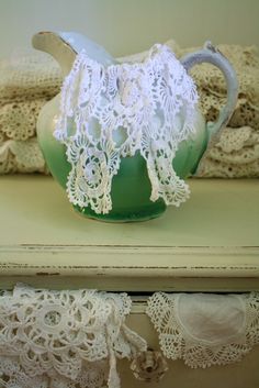 a green pitcher with white lace on it sitting on a table next to doily