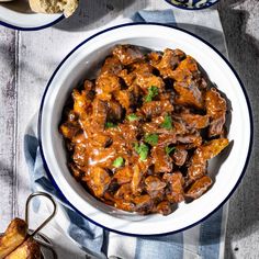 a bowl filled with meat and sauce on top of a blue and white table cloth