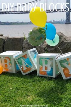 an image of baby blocks on the grass with balloons in front of water and bridge