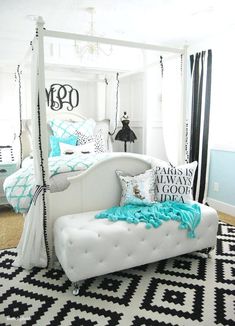 a white bed with blue and black pillows on top of it next to a chandelier