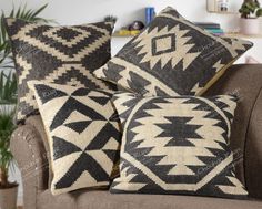 three black and white pillows sitting on top of a brown couch next to a potted plant