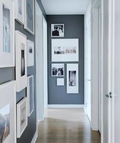 a long hallway with pictures on the wall and wooden flooring, along with white framed photos