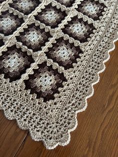 a crocheted blanket is laying on the floor next to a wooden floor with a brown and white afghan