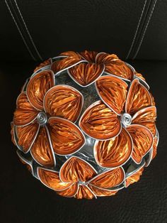 an orange and silver object is hanging on a black leather surface in the shape of a flower