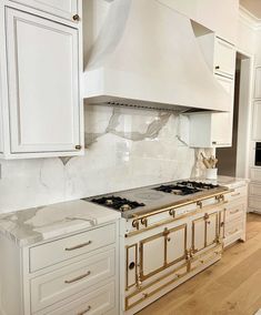 a white kitchen with marble counter tops and gold trim on the oven hood, cabinets, and drawers